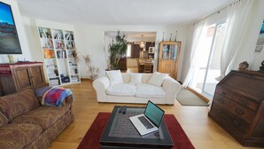 A living room with a sofa, a coffee table with a laptop, a bookshelf, and a dining area in the background. - Beautiful large 3 bedroom apartment, terrace sea views, Wifi. (Tarifa)