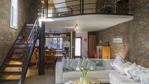 Een ruime loft met een hoogslaper, een trap, een eethoek en een woonkamer met een bank en salontafel.