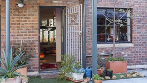 Een bakstenen gebouw met een houten deur, bloempotten en een kleine tuin.