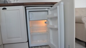 Un petit réfrigérateur doté d’un compartiment congélateur, situé dans un petit espace cuisine avec un revêtement de sol à motifs.