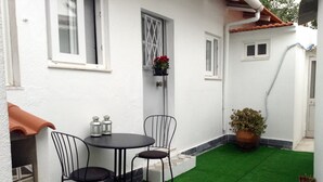 Une petite terrasse avec une table ronde et deux chaises, entourée de murs blancs et d’une zone recouverte de gazon synthétique vert.