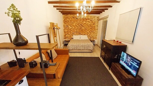Une chambre à coucher de taille réduite, avec un lit, un téléviseur et un mur en briques.