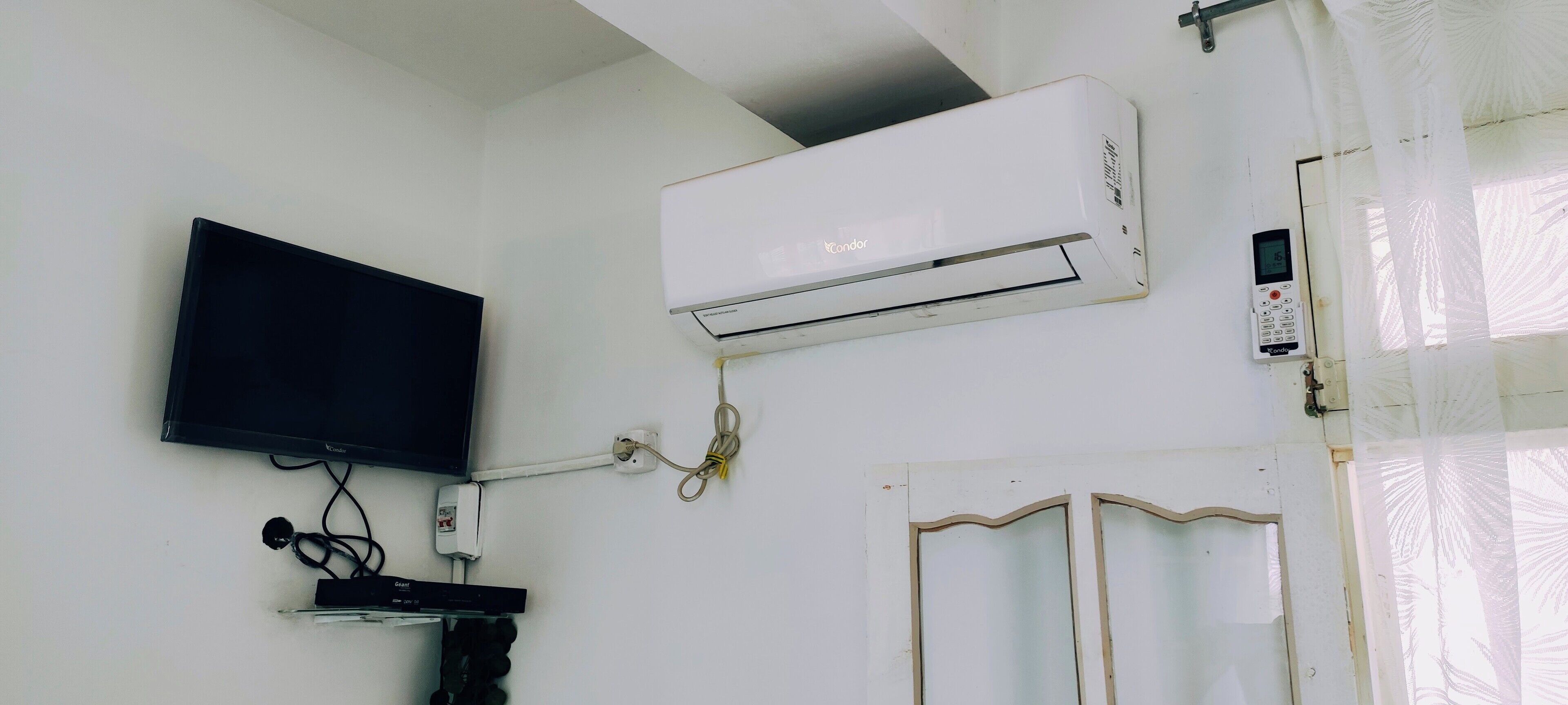 A room with a mounted air conditioner, a flat-screen TV, and a door with a decorative frame.