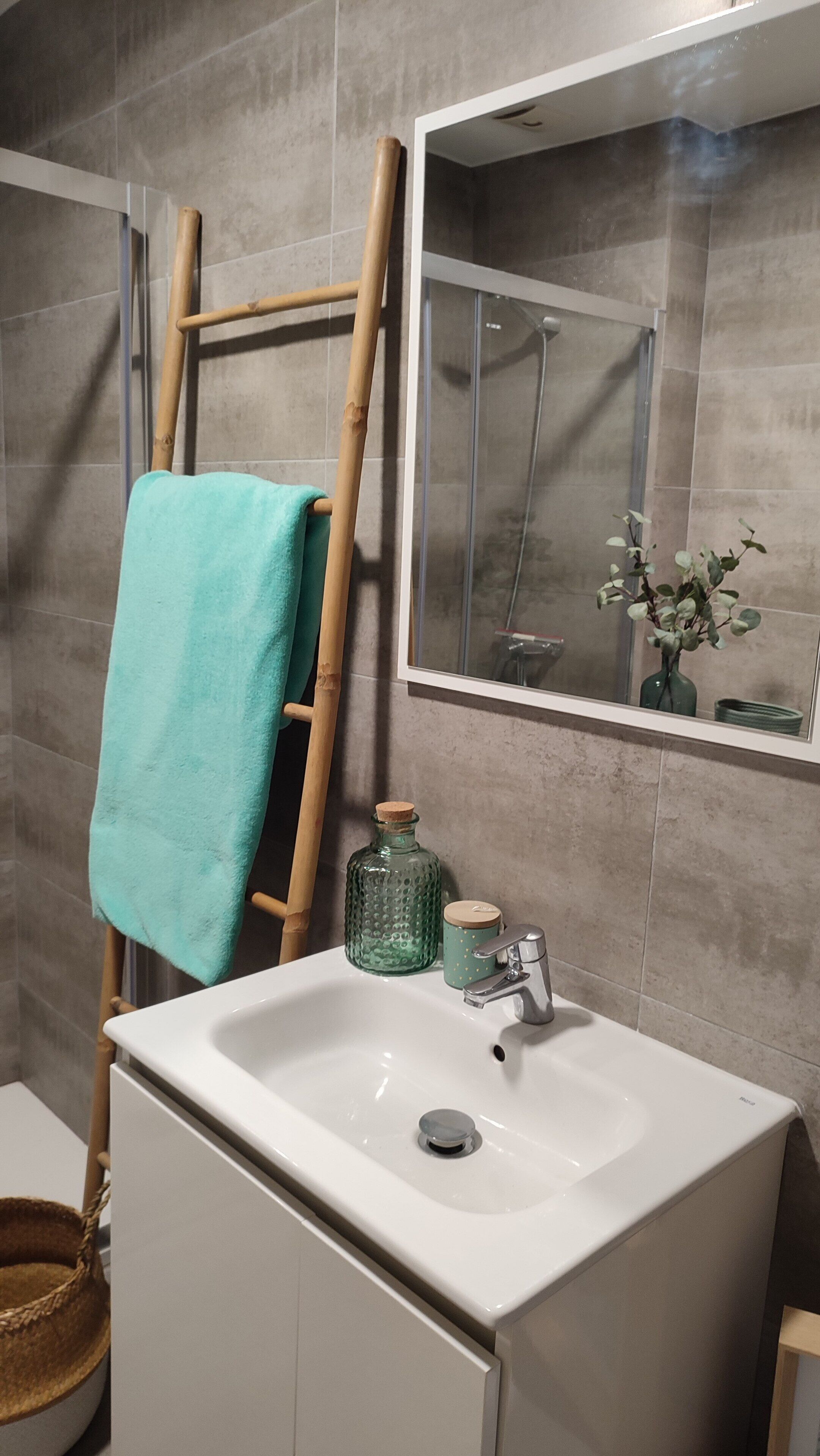 A bathroom with a white sink, a mirror, a towel rack, a green bottle, and a wooden ladder.