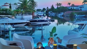 En småbåtshamn med förtöjda båtar, en pool med glasbotten och solstolar.