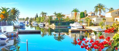 A marina with boats docked, surrounded by palm trees and houses.