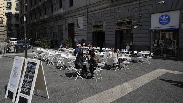 An outdoor seating area with tables and chairs arranged in front of a building with an Adidas store. - Jeancarlos House in the historic center (Napoli)