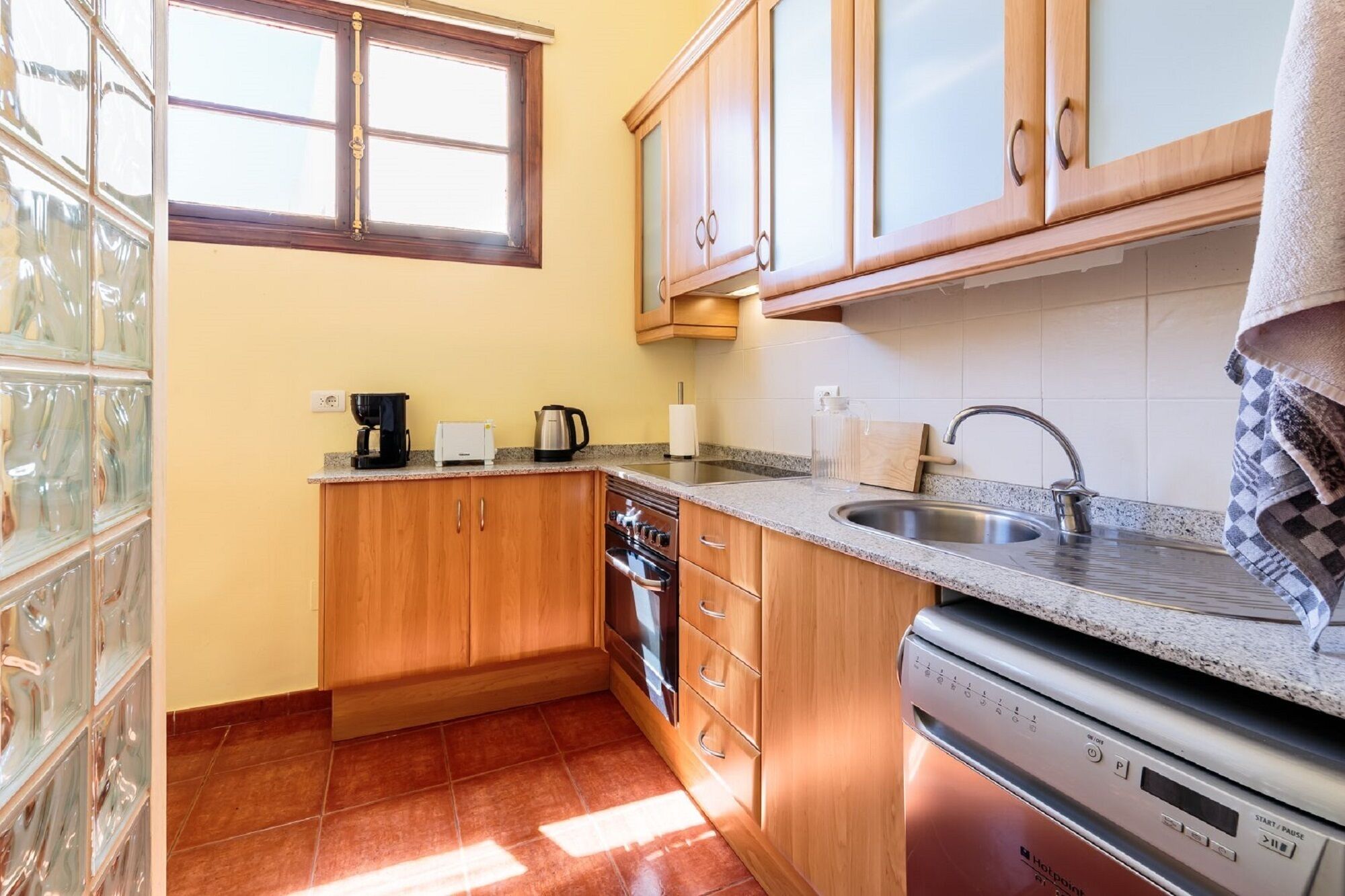 Una cocina compacta con armarios de madera, horno empotrado, lavavajillas y encimera de granito.