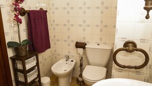 Un baño con bidé, inodoro, lavabo y una repisa con una planta y toallas.