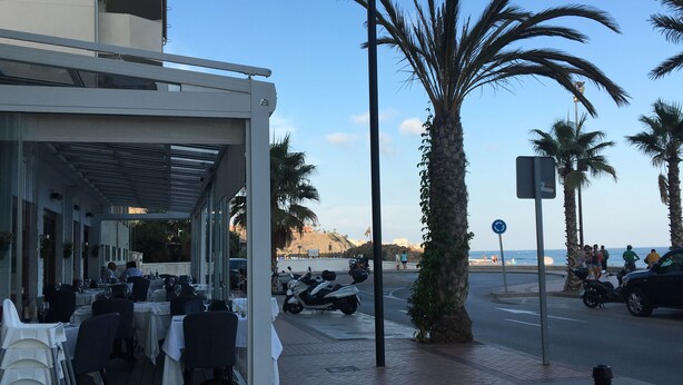 An outdoor restaurant with tables and chairs, palm trees, and a view of the beach and ocean. - Beautiful Flat in Fuengirola with terrace sea view and 2 minutes from the beach  (Fuengirola)