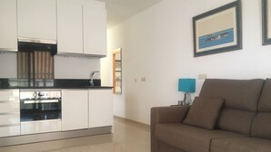 A modern kitchen with white cabinets and a built-in oven, a brown sofa in the living area, and a framed picture on the wall. - Beautiful Flat in Fuengirola with terrace sea view and 2 minutes from the beach  (Fuengirola)