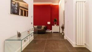 A modern living room with a red accent wall, a glass coffee table, a sofa, and a white radiator. - n'apARTment - art in the heart of Naples (Napoli)