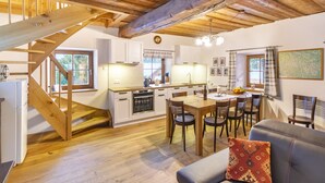 Una cocina acogedora con vigas de madera, una zona de comedor con mesa y sillas, y una escalera que sube a otro nivel.