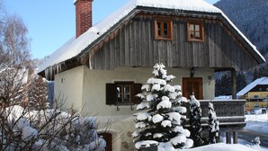 Una casa de madera con techo inclinado cubierto de nieve, una chimenea y una ventana con contraventanas.