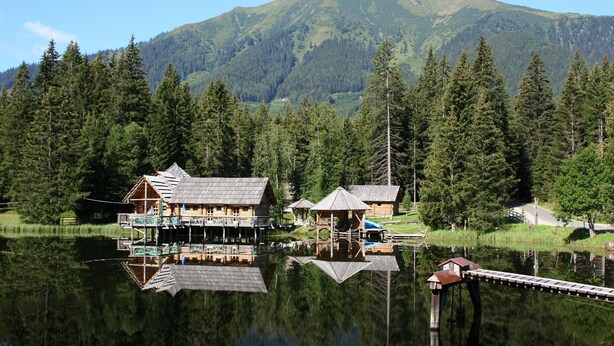 Un alojamiento junto al lago con cabañas de madera, un muelle y montañas al fondo.