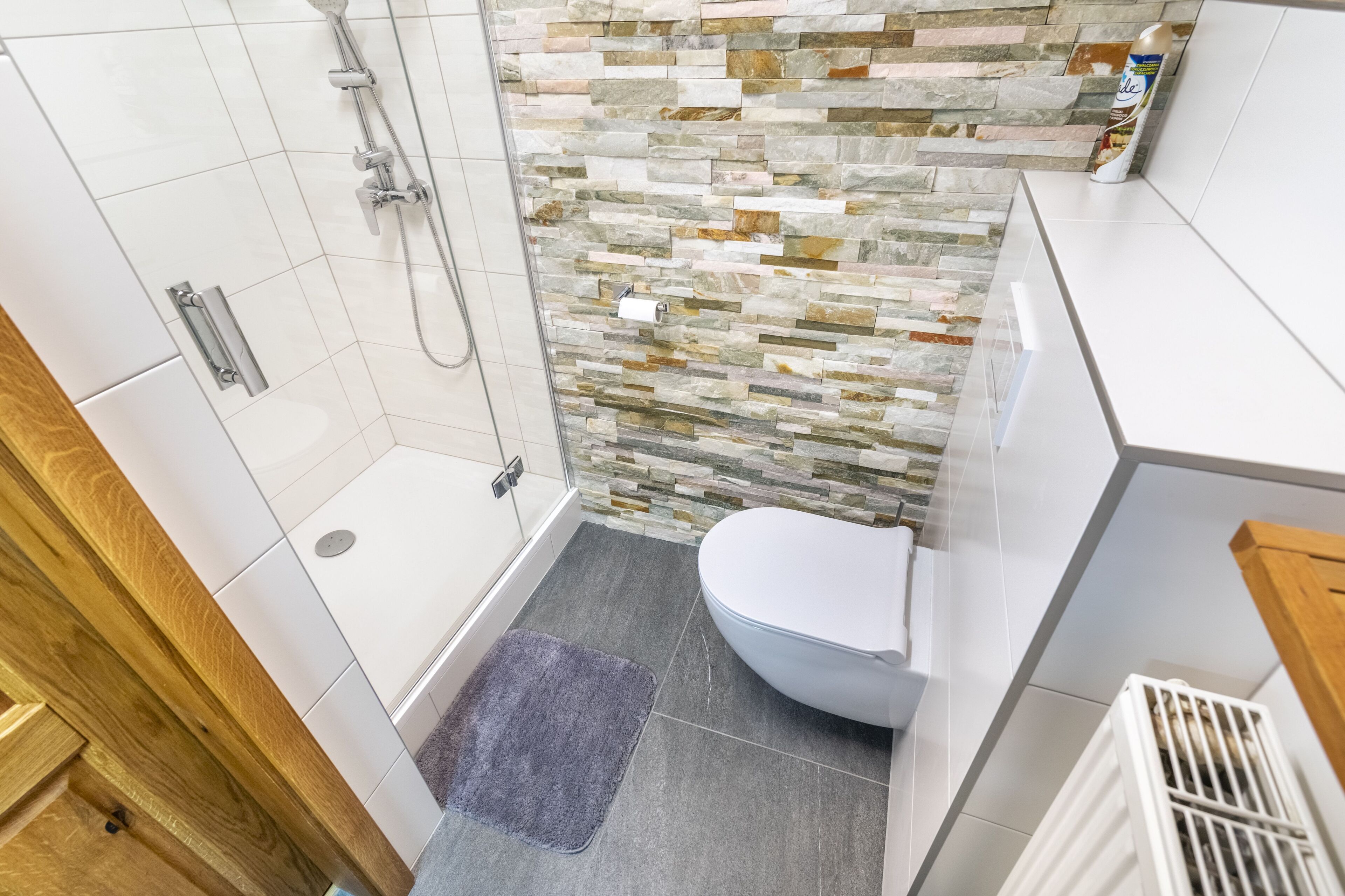Une salle de bain moderne avec douche, toilettes et un mur décoré d’une mosaïque de pierres.