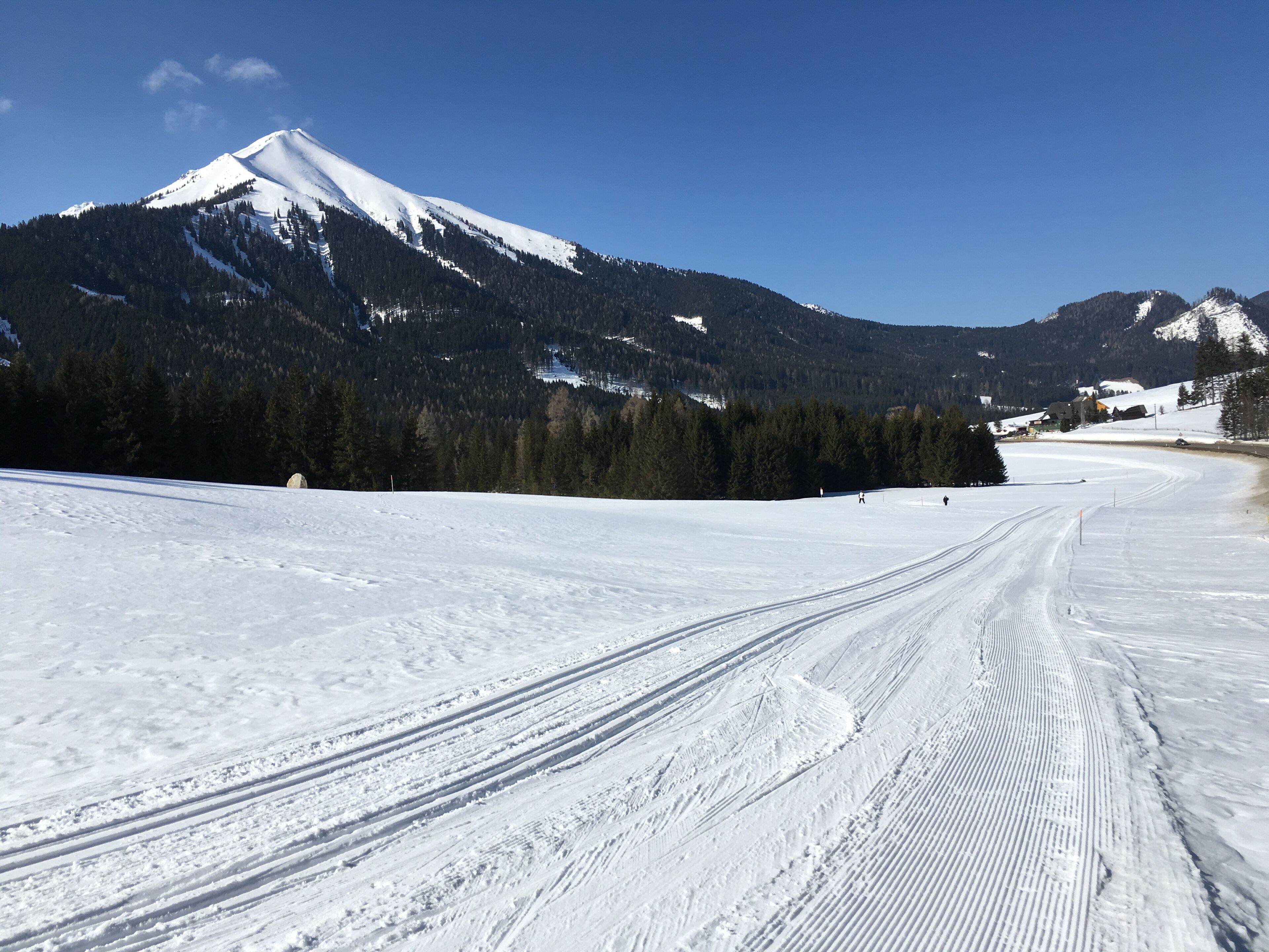 A snow-covered ski slope with tracks and a mountain in the background.