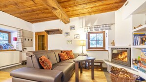 Una sala de estar acogedora con un sofá de cuero, una chimenea, vigas de madera en el techo y una estantería.