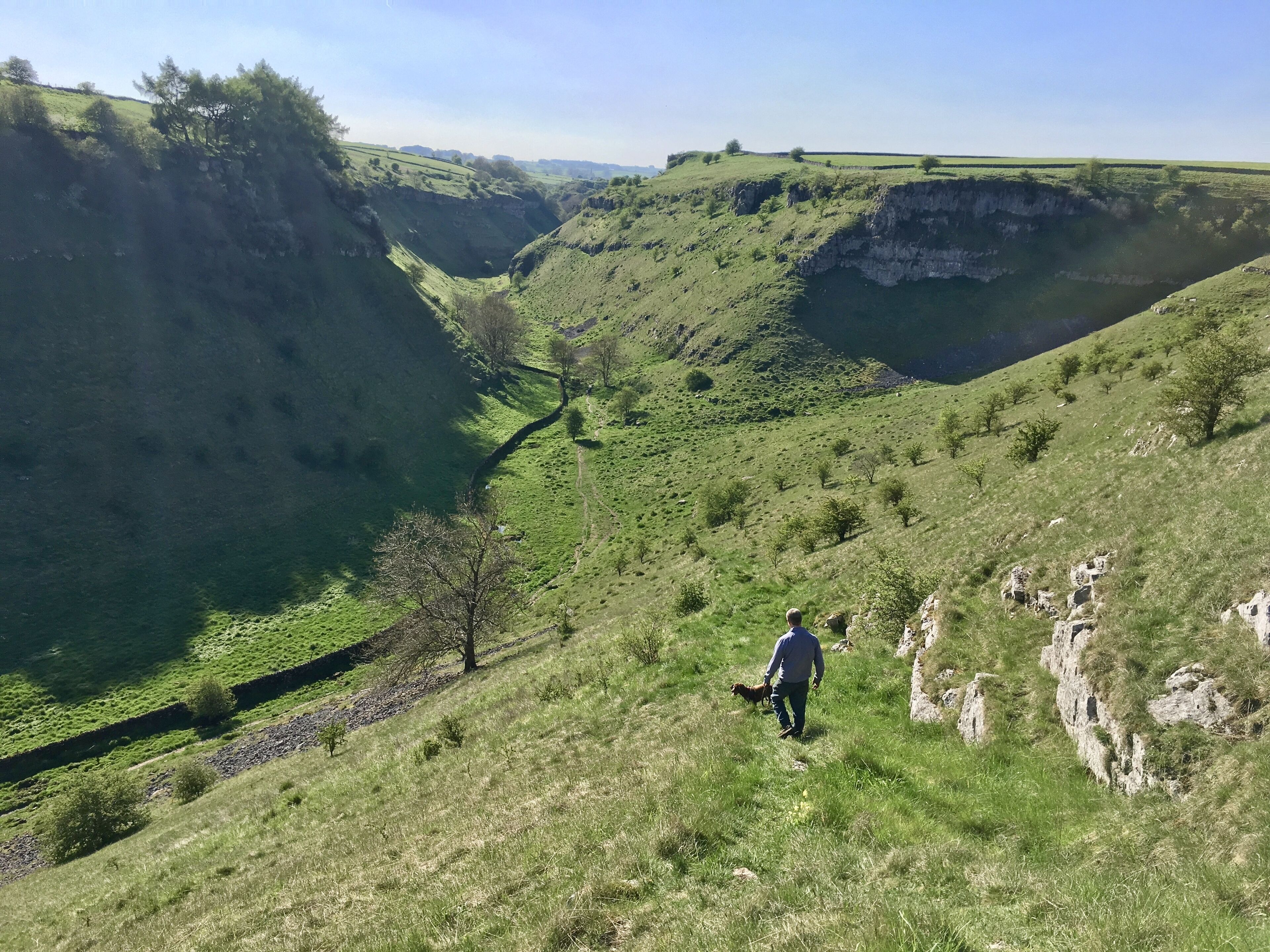 A person walking on a grassy hillside with a valley in the background.