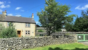 A stone wall with a grassy area in front of a two-story house with a chimney. - Characterful , pet friendly cottage ,sleeps 4 ,stunning views ,village location. (Biggin)
