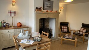A cozy living room with a fireplace, a dining table with chairs, and a comfortable seating area with a sofa and armchairs. - Characterful , pet friendly cottage ,sleeps 4 ,stunning views ,village location. (Biggin)