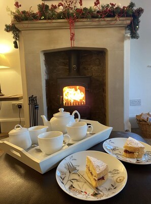 A cozy room with a fireplace, a tray with white teacups and a teapot, and plates with food.