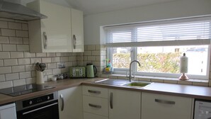 A modern kitchen with white cabinets, a stainless steel oven, a built-in dishwasher, a window with blinds, and a green toaster. - Characterful , pet friendly cottage ,sleeps 4 ,stunning views ,village location. (Biggin)