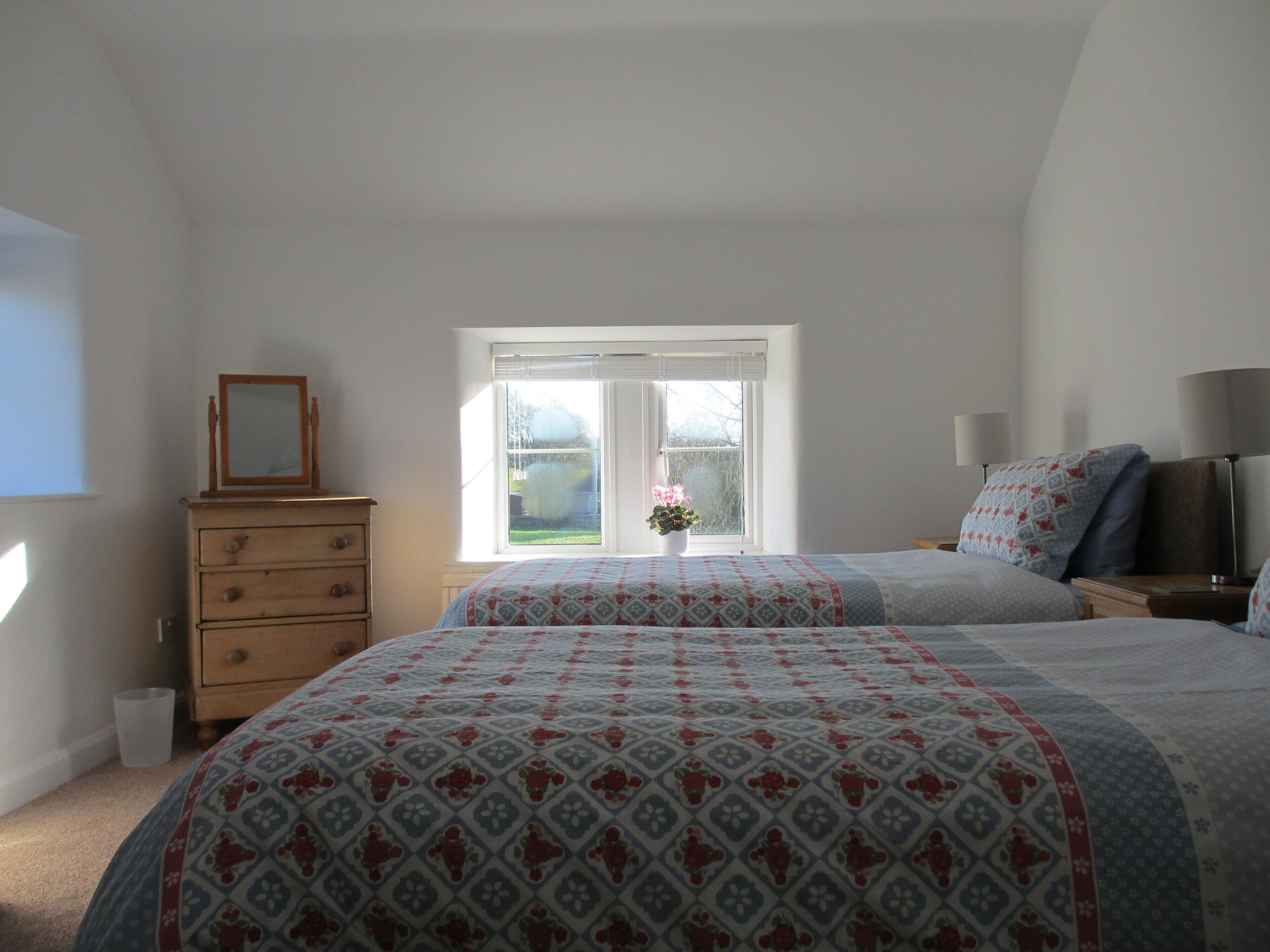 A bedroom with two beds, a dresser, a window with a view, and a bedside table with lamps.