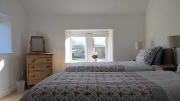 A bedroom with two beds, a dresser, a window with a view, and a bedside table with lamps.