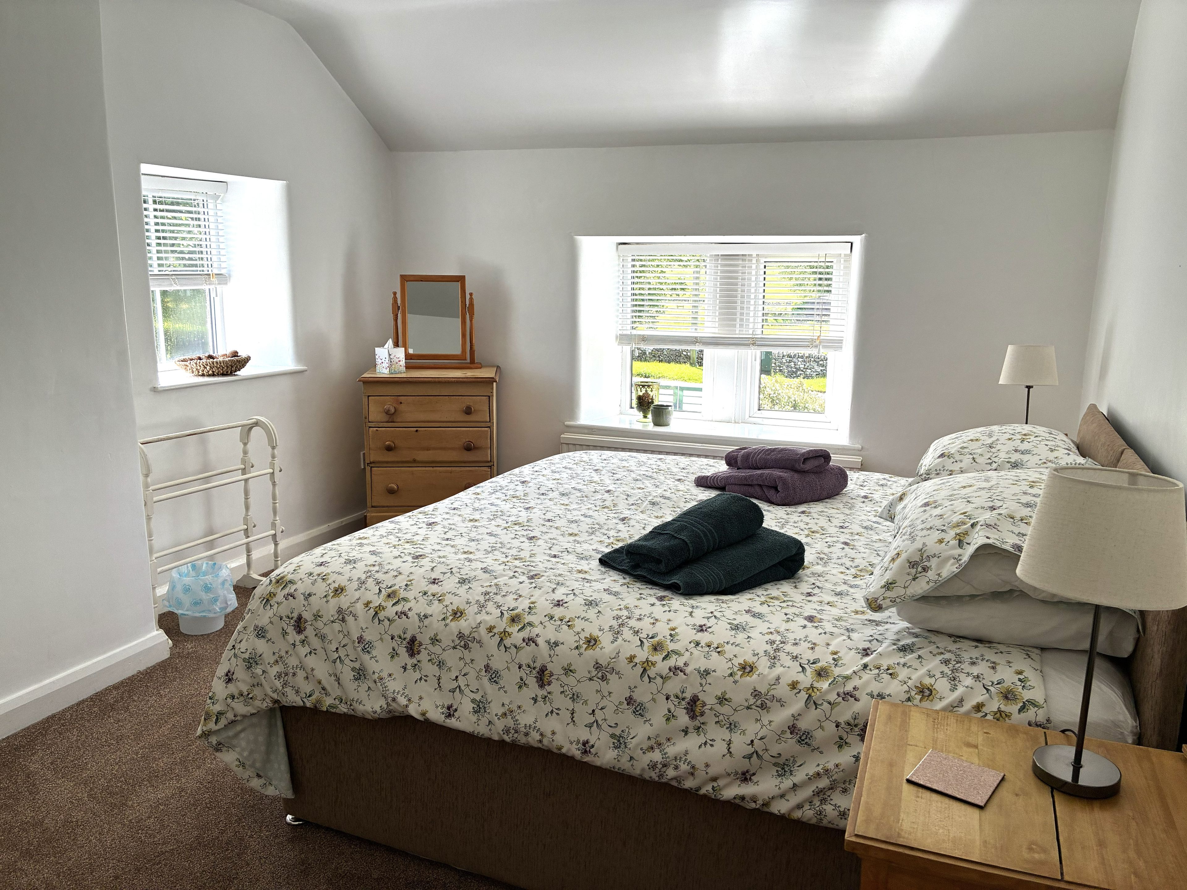 A bedroom with a bed, dresser, window, and bedside table.