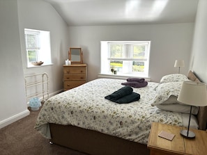 A bedroom with a bed, dresser, window, and bedside table. - Characterful , pet friendly cottage ,sleeps 4 ,stunning views ,village location. (Biggin)