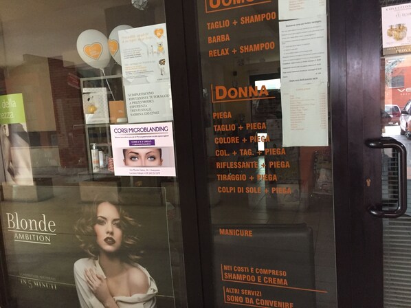 A salon interior with various hair and beauty treatments listed on the glass door, including microblanding and manicures.
