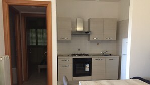 Una cocina compacta con estufa, fregadero y lavavajillas. En primer plano, una mesa de comedor con sillas.