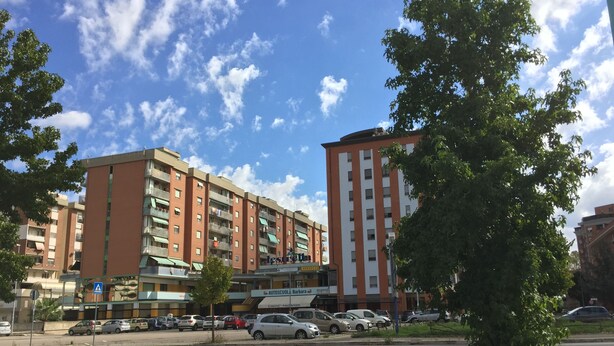 Un edificio de varios pisos con fachada roja y color crema, varios balcones y un estacionamiento lleno de autos.