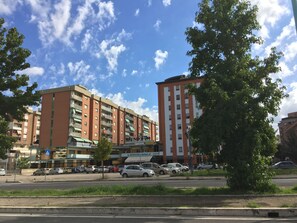 En byggnad med flera våningar, en röd och beige fasad, flera balkonger och en parkeringsplats med bilar.