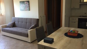 Una sala de estar moderna con un sofá gris, una mesa de comedor con una caja negra y una cesta, y un área de cocina con armarios y una estufa.