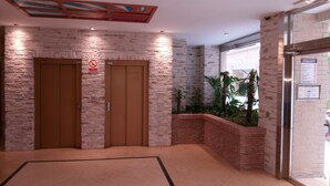 An elevator area with two wooden doors, a stone wall, a small planter with plants, and a glass door to the right.