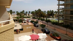A balcony with a view of a beach, palm trees, and a parking area with cars.
