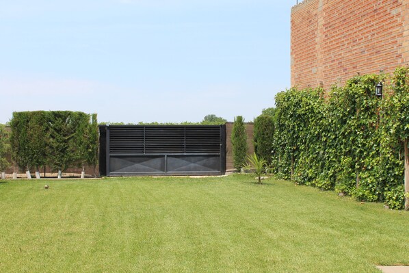 A modern building with a large garage door, surrounded by well-maintained grass and hedges. - AN ALTERNATIVE ON GAUDIR D'UN ESPAI COMÚ FAMILIAR FOLLOWS LA SEVA FINALITAT (El Tarros)
