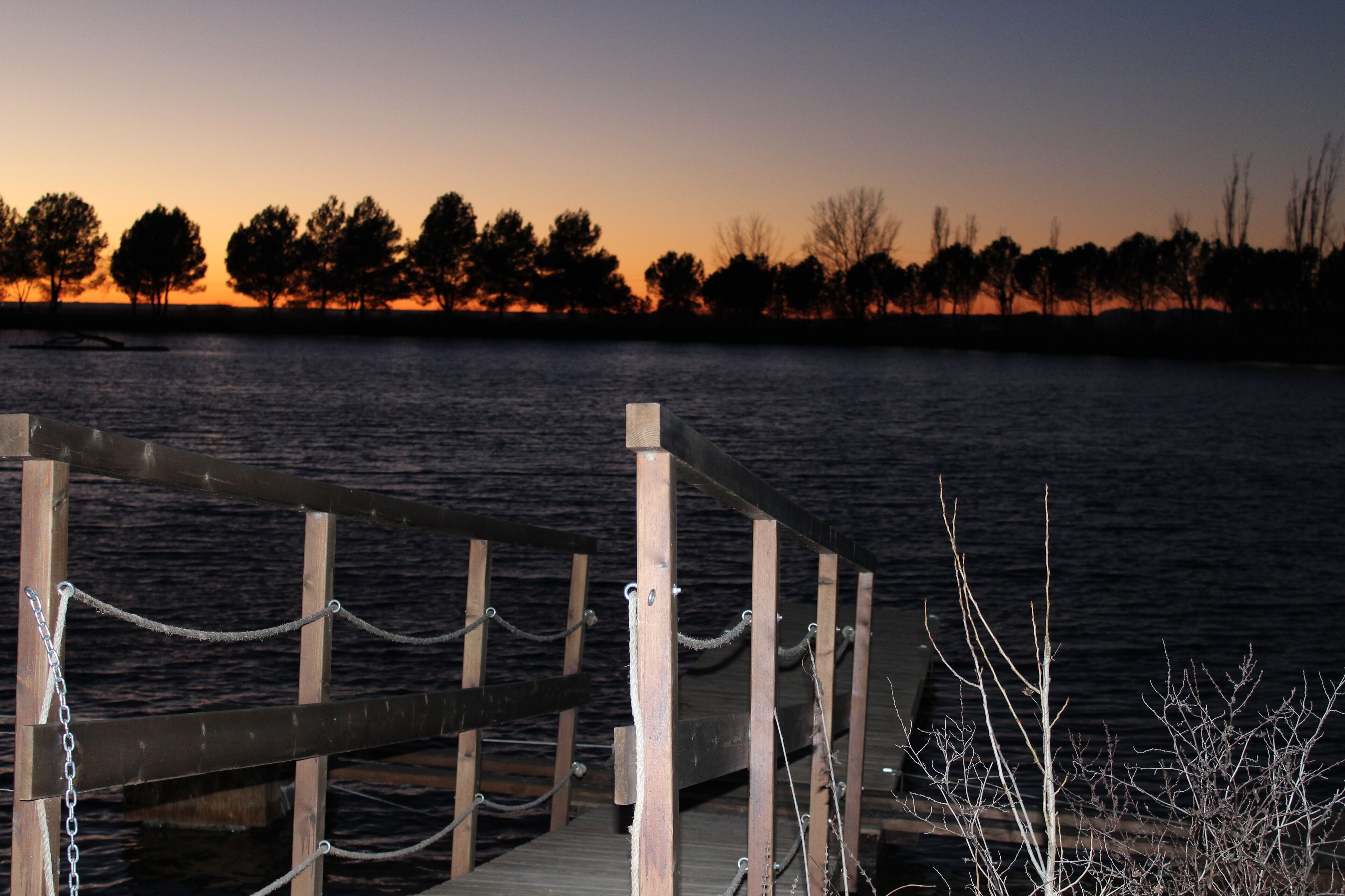 Une jetée en bois, avec des chaînes, qui mène à une étendue d’eau au coucher du soleil.