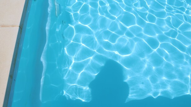 Ein klares, blaues Schwimmbecken mit sichtbaren Wellen und Spiegelungen auf der Wasseroberfläche.