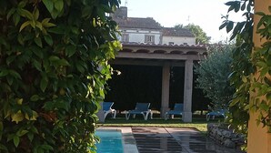 Ein überdachter Außenbereich mit Pool, Liegestühlen und einer Steinmauer.