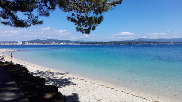 A beach with clear turquoise water, a sandy shore, and a distant cityscape.