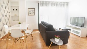 A modern living room with a sofa, a dining table with chairs, a TV, and a bookshelf.
