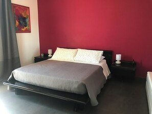 Une chambre à coucher moderne avec un lit, deux tables de chevet et un mur d’accent rouge.