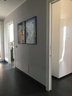 Un couloir avec un plancher sombre, une porte blanche et deux œuvres d’art encadrées accrochées au mur.