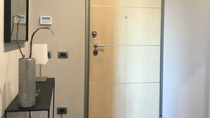 Une chambre moderne avec une porte en bois, une petite table sur laquelle est posé un vase, et un luminaire fixé au mur.