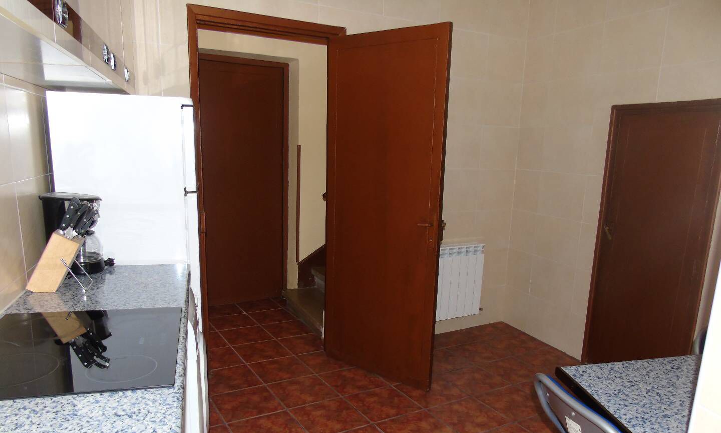 Una cocina con encimera negra, puerta de madera y suelo de baldosas.