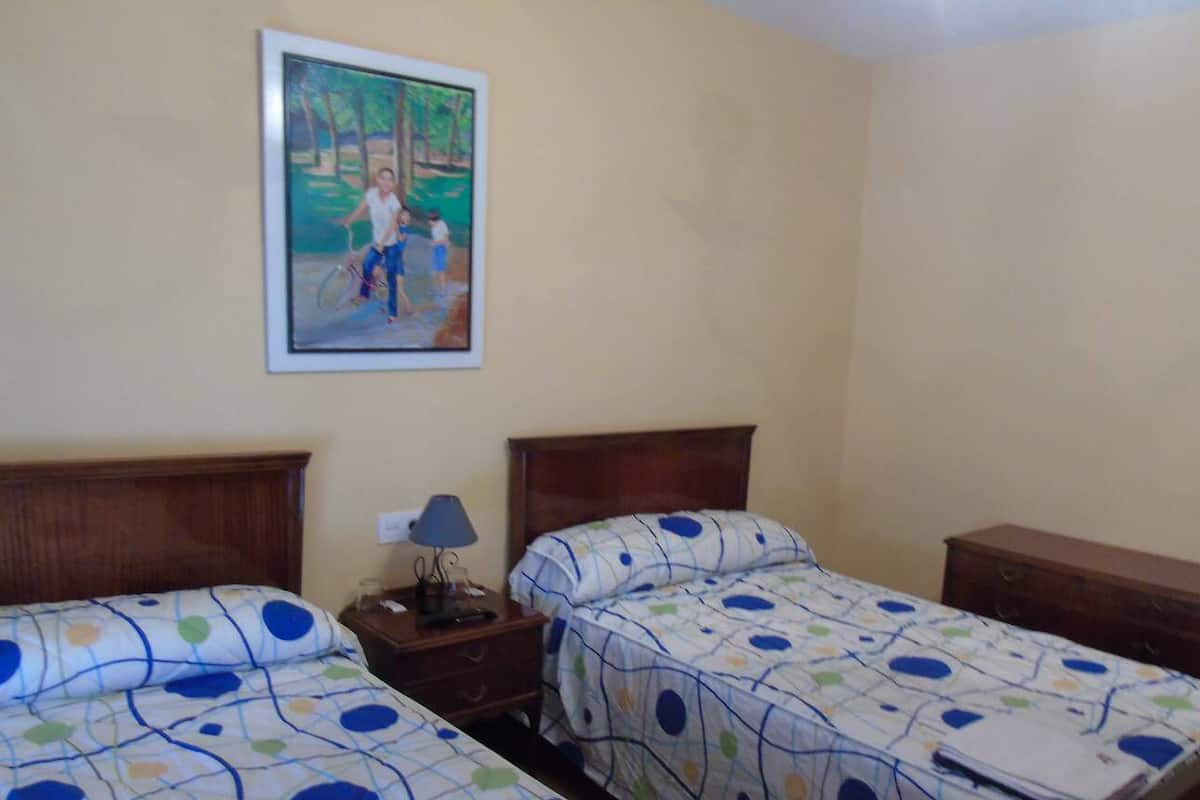 Un dormitorio con dos camas individuales, una mesita de noche con lámpara y un cuadro en la pared.