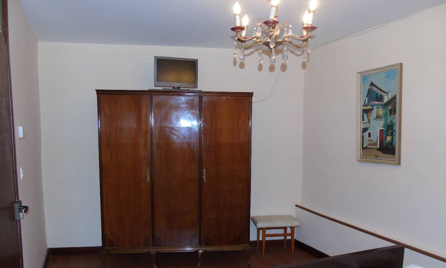 Una habitació amb un armari de fusta, una petita banca, un quadre a la paret i un lampadari.